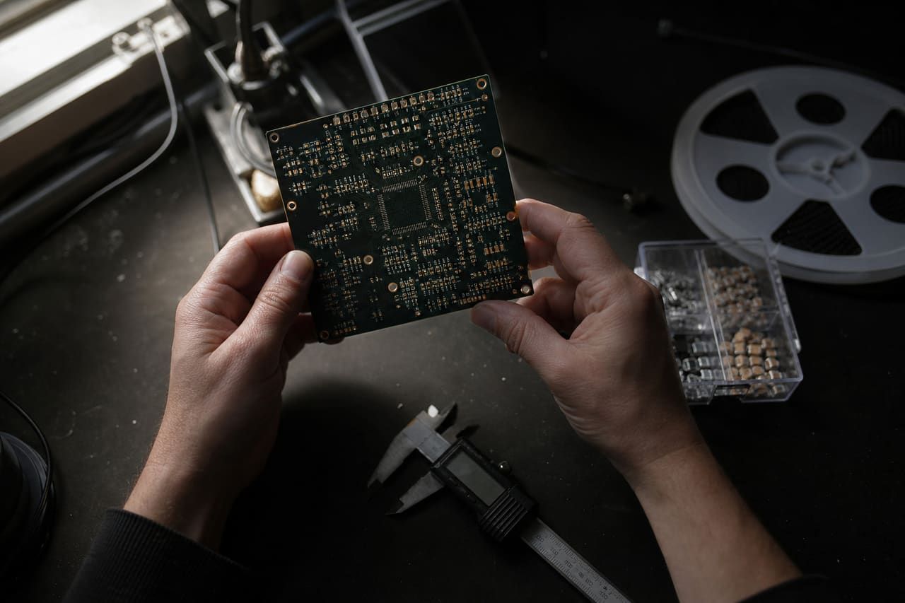 Engineer inspecting a bare printed circuit board by hand, digital callipers and component reels on the bench